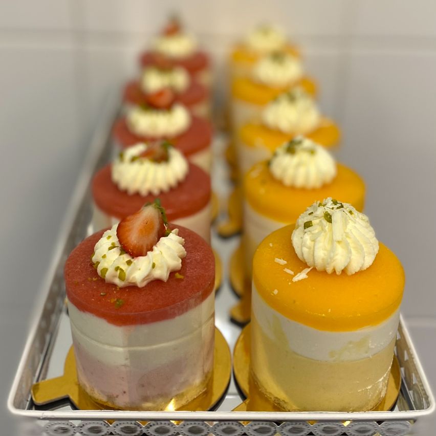 Ein Tablett mit verschiedenen kleinen Desserts, einschließlich Erdbeere und Mango mit weißer Creme, auf einem silbernen Tablett angeordnet.