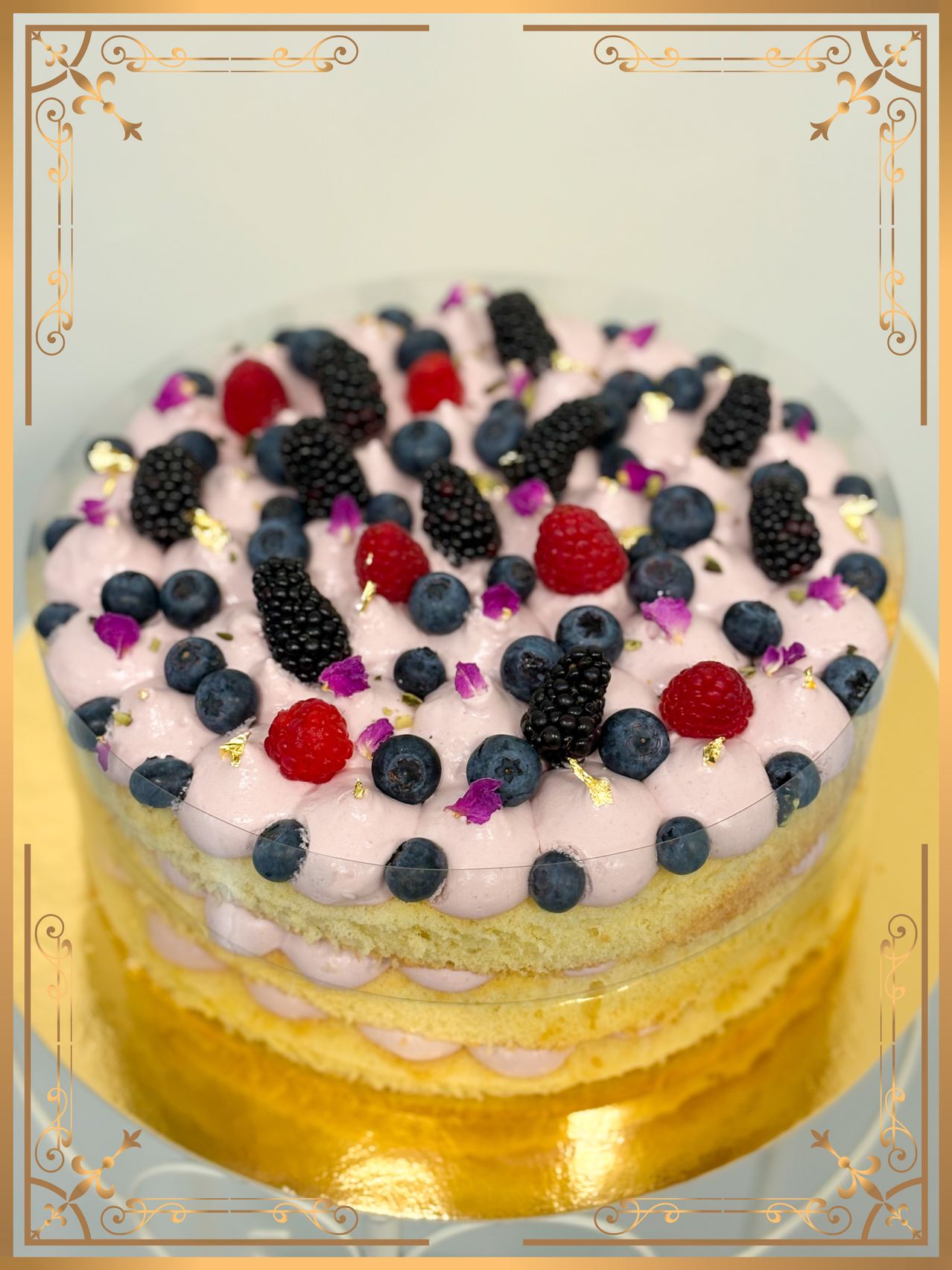 Ein mehrschichtiger Kuchen mit weißer Glasur, oben mit Brombeeren, Blaubeeren und Himbeeren verziert, verziert mit essbaren Blumen und Goldpartikeln.