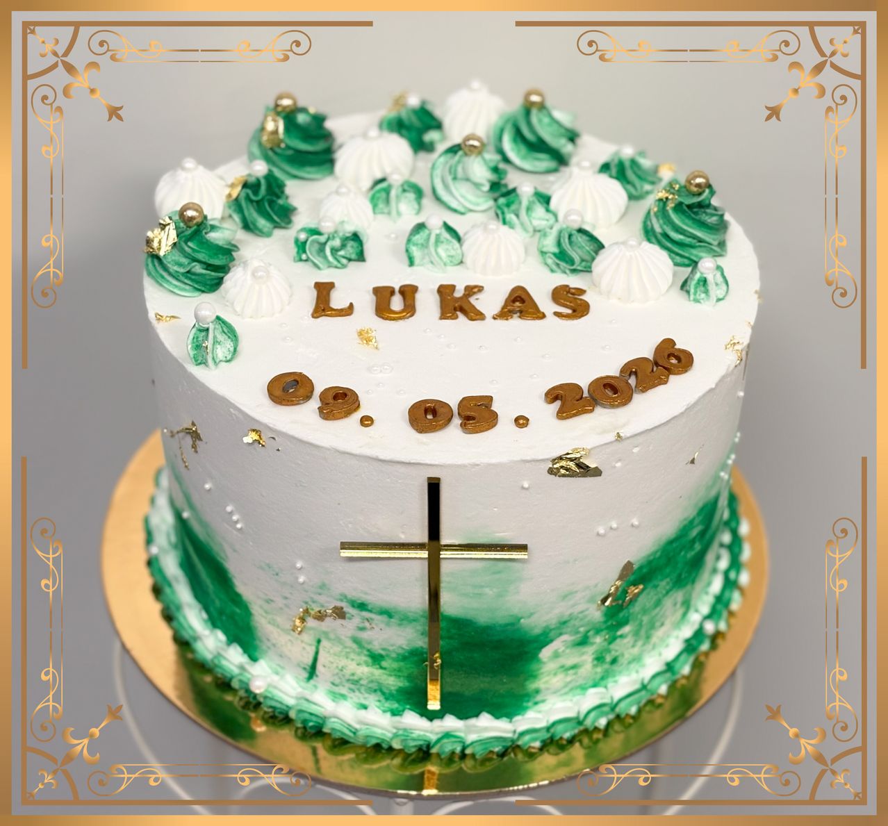 A white cake with green frosting and white icing decorations, a gold cross in the center, and the name Lukas and date 09.05.2020 written on it.
