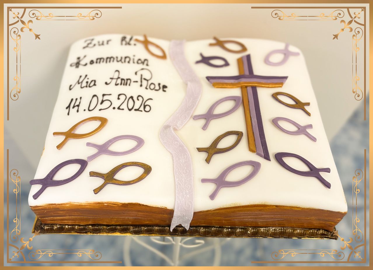Ein Kuchen, der als offenes Buch dekoriert ist, mit Kreuz- und Fischsymbolen. Der Kuchen ist für Mia Ann-Roses Kommunion am 14. Mai 2026.