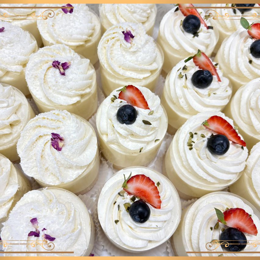 Eine Nahaufnahme mehrerer weißer Sahnecreme-Gebäcke mit Erdbeer- und Blaubeer-Toppings. Jedes Gebäck hat eine Wirbel aus Schlagsahne und eine dekorative Blume obenauf.