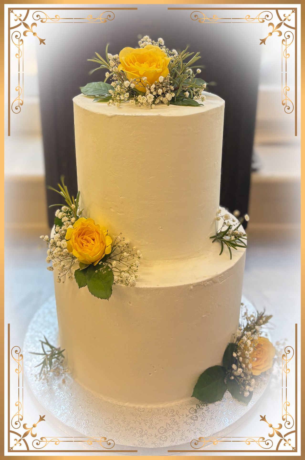 A three-tier cream cake with yellow roses and baby's breath on a white cake stand, with a blurred background.