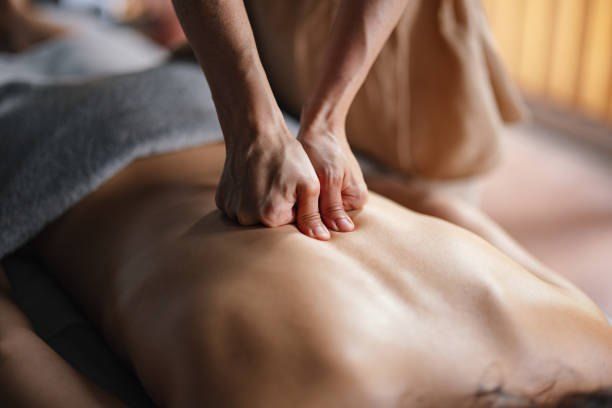 Eine Person liegt auf einem Bett und bekommt von jemandem, der Shorts trägt, eine Rückenmassage.