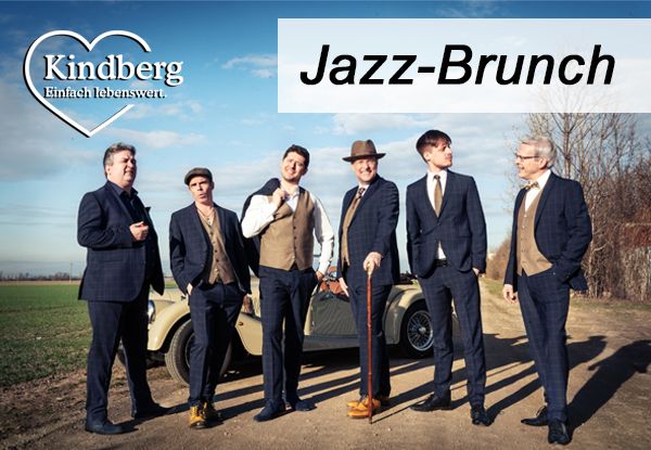 Fünf Männer in Anzügen und Hüten posieren für ein Foto vor einem Oldtimer, mit einem Feld und Bäumen im Hintergrund.