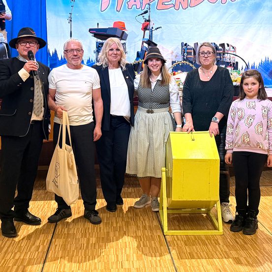 Eine Gruppe von Menschen posiert für ein Foto vor einer gelben Box. Dahinter ein Banner mit dem Text 'JAPENDOR'. Ein Mann hält ein Mikrofon.