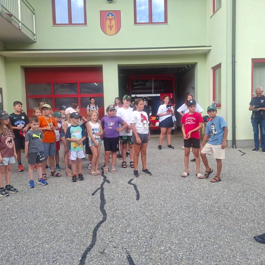 Eine Gruppe von Kindern und Erwachsenen steht vor einer Feuerwehrwache mit einem Feuerwehrauto im Inneren.