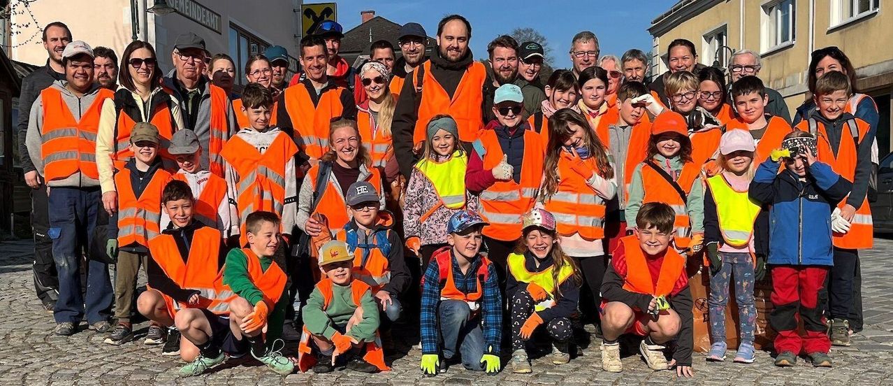 Eine Gruppe von Menschen, die Warnwesten und Handschuhe tragen, lächeln und für ein Foto auf einer Kopfsteinpflasterstraße posieren.