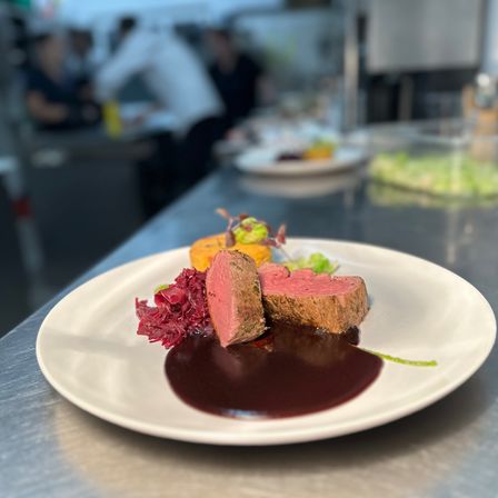 Ein Gourmet-Gericht mit Fleisch, Rotkohl und Soße auf einem weißen Teller in einer Küche.