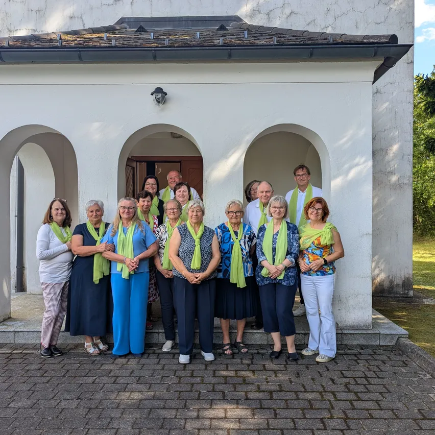 Eine Gruppe von Menschen mit grünen Schals posiert für ein Foto vor einem weißen Gebäude.