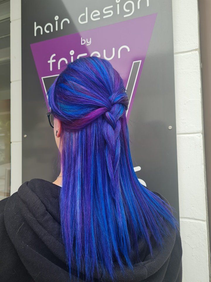 Eine Person mit langen, lebhaften blauen Haaren in einer Zöpfe steht vor einem Schild.