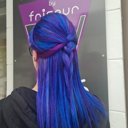 Eine Person mit langen, lebhaften blauen Haaren in einer Zöpfe steht vor einem Schild.