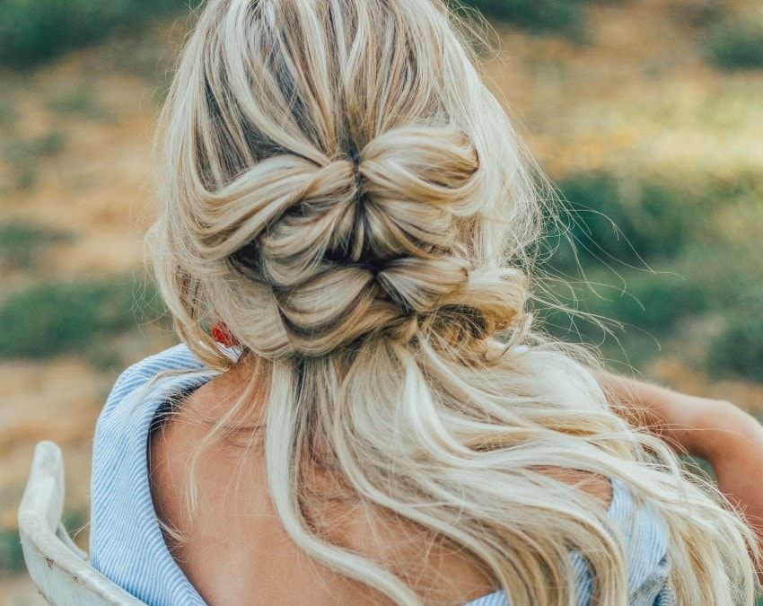 Rückansicht einer Frau mit langen blonden Haaren, die zu einem doppelten Dutt gestylt sind. Sie trägt ein blaues Oberteil.