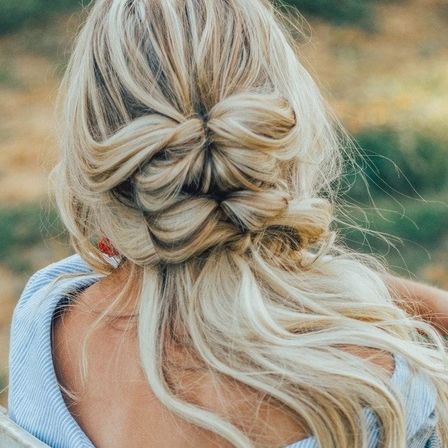 Rückansicht einer Frau mit langen blonden Haaren, die zu einem doppelten Dutt gestylt sind. Sie trägt ein blaues Oberteil.