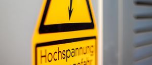Ein gelbes Schild mit einem schwarzen Pfeil nach unten und den Worten Hochspannung Lebensgefahr.