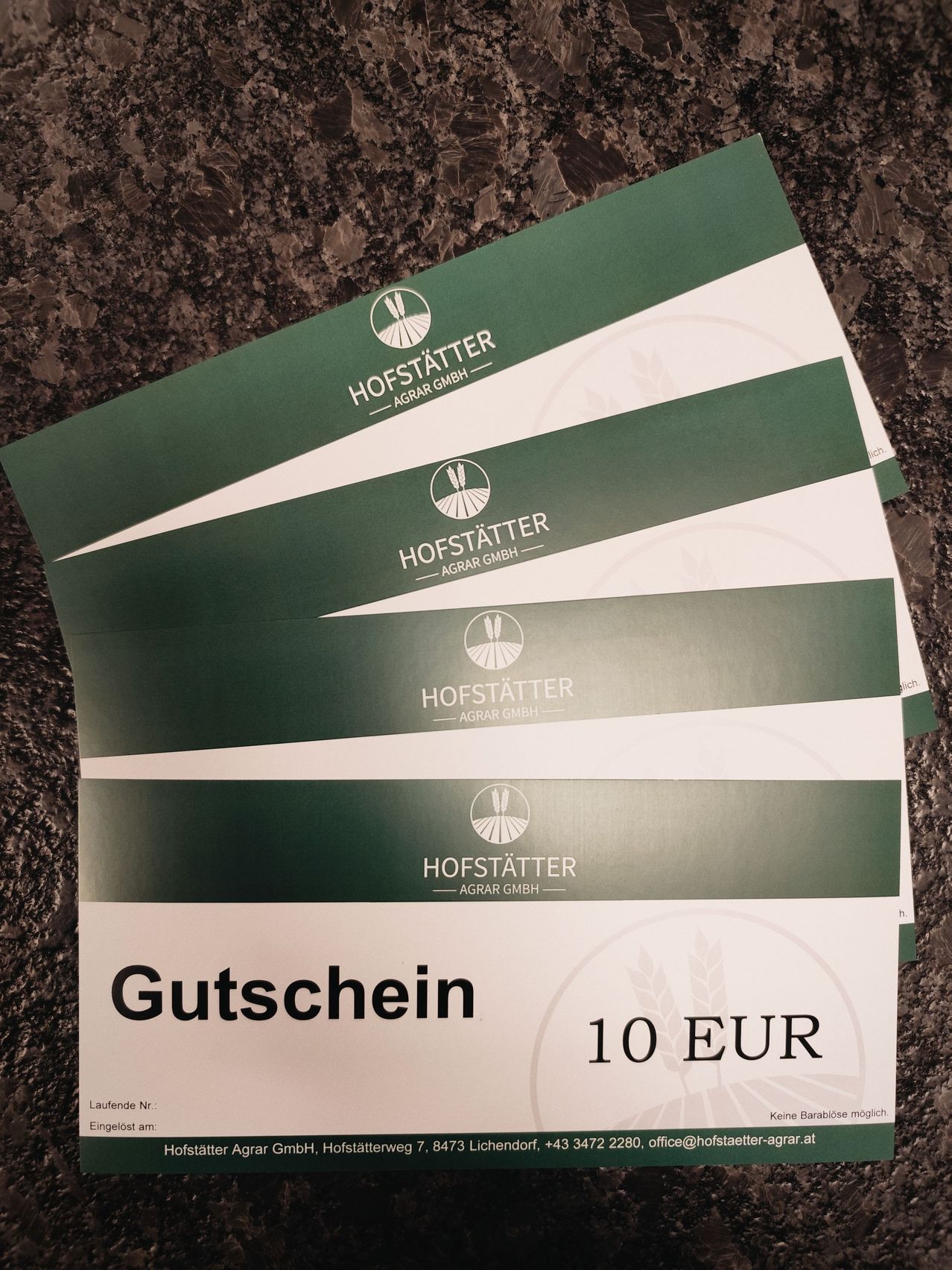 Gestapelte Gutscheine von Hofstatter Agrar GmbH, jeweils im Wert von 10 EUR, auf einer Marmoroberfläche ausgestellt.