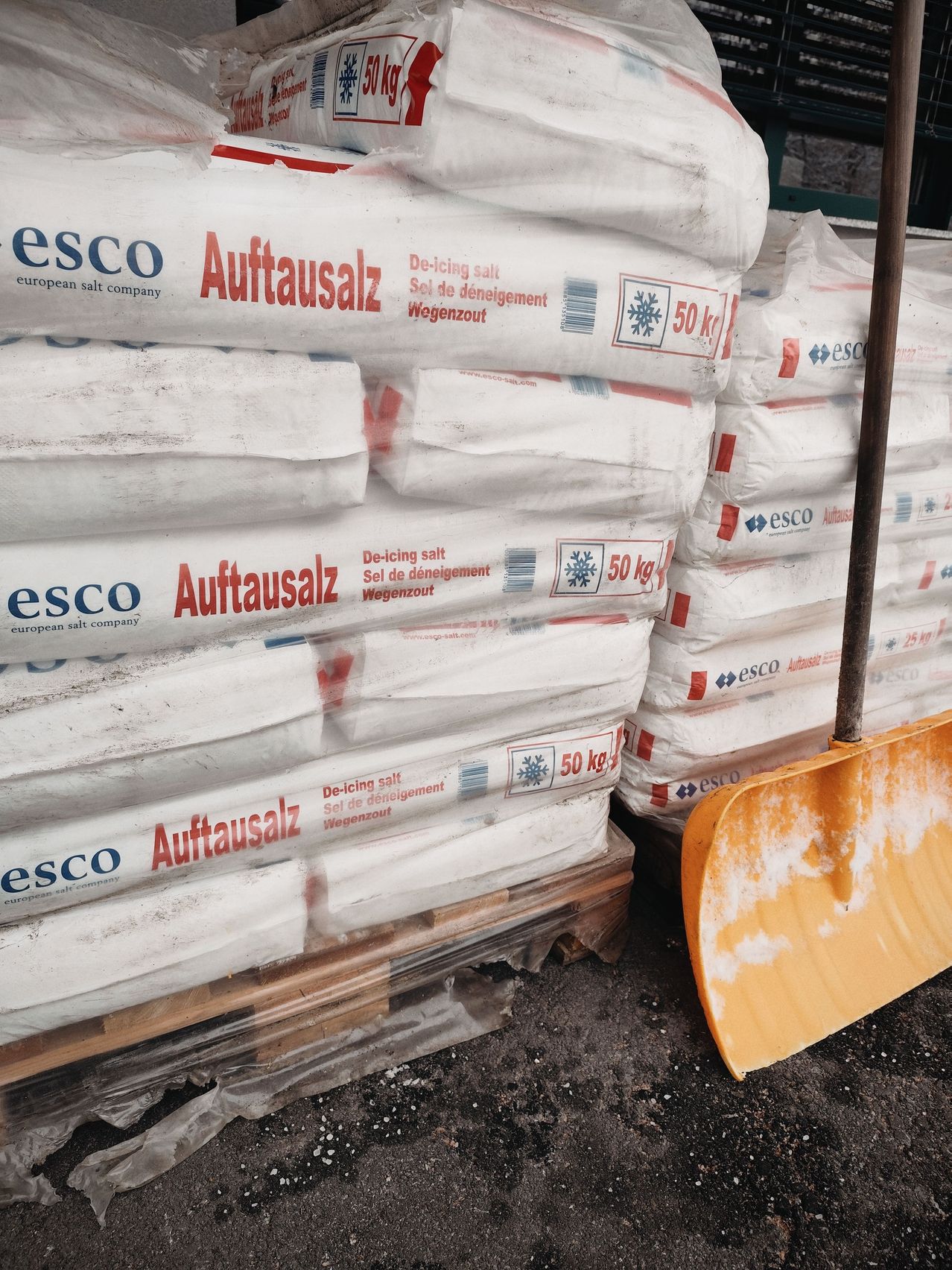 Gestapelte Säcke mit Auftausalz, beschriftet mit Auftausalz, mit einer gelben Schaufel im Vordergrund.