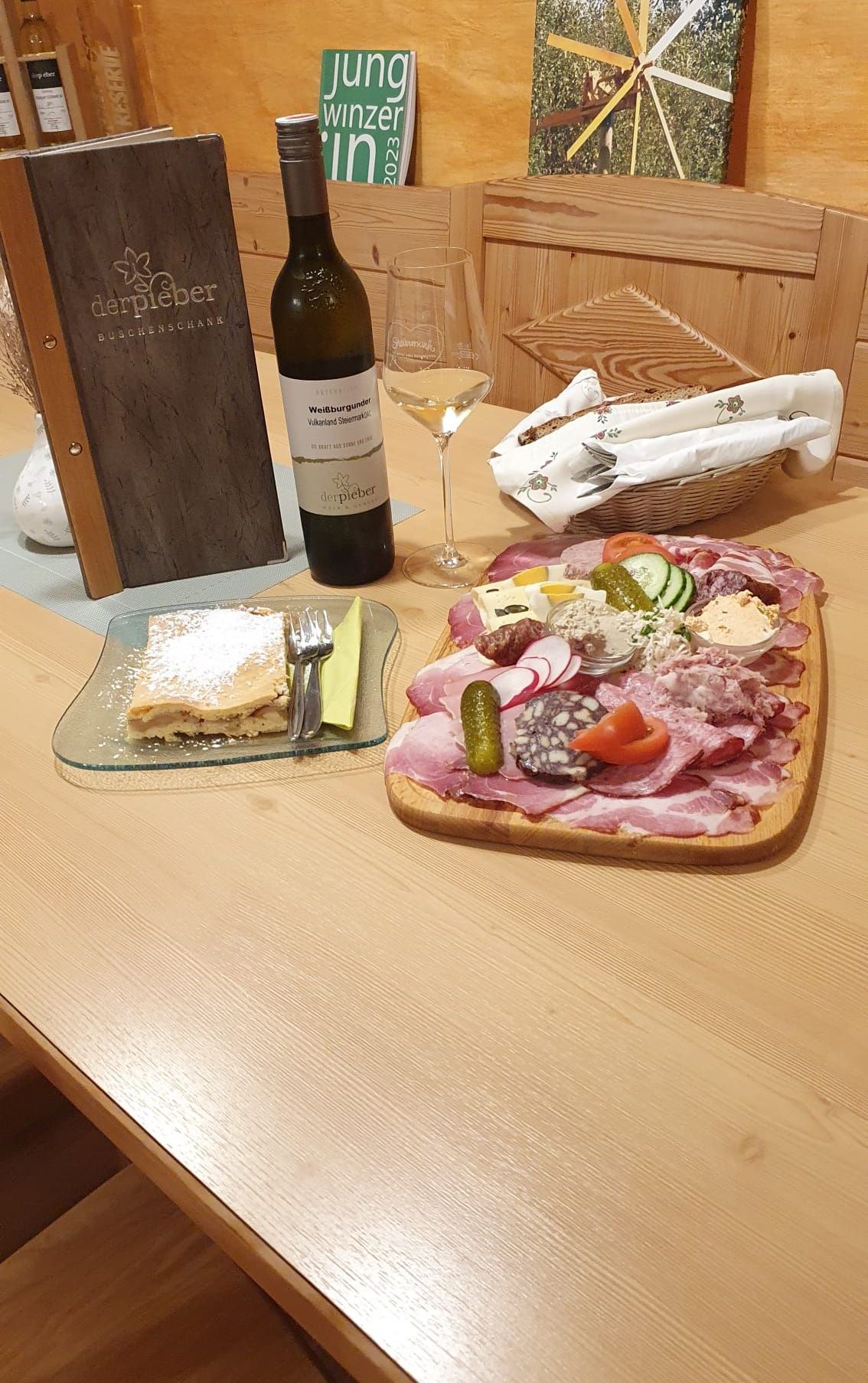 Ein Holztisch mit Käseplatte, einem Teller mit Dessert, einer Weinflasche und einem Weinglas.