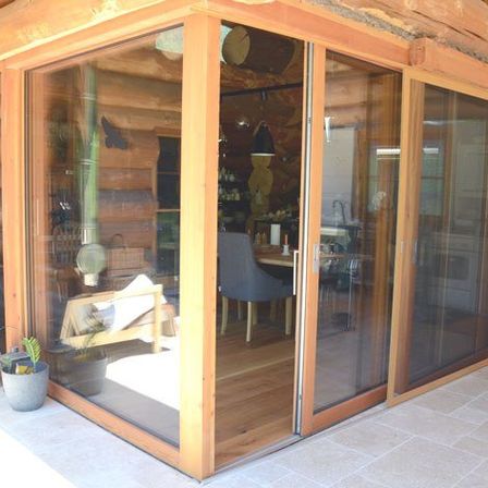 Ein gemütliches Blockhaus-Interieur mit Holzwänden, Schiebetüren aus Glas und einem Holzboden. Es gibt einen Tisch mit einem Stuhl, einem Topf und einem Fahrrad.