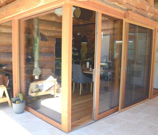 Ein gemütliches Blockhaus-Interieur mit Holzwänden, Schiebetüren aus Glas und einem Holzboden. Es gibt einen Tisch mit einem Stuhl, einem Topf und einem Fahrrad.