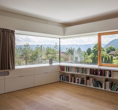 Ein Zimmer mit einer großen Fensterbank, gefüllt mit Büchern, und Blick auf eine Berglandschaft.