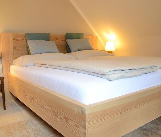 Ein ordentlich gemachtes Bett mit weißer Bettwäsche und Kissen, Holzbettrahmen und zwei Lampen auf beiden Seiten. Ein Holzstuhl ist neben dem Bett platziert.