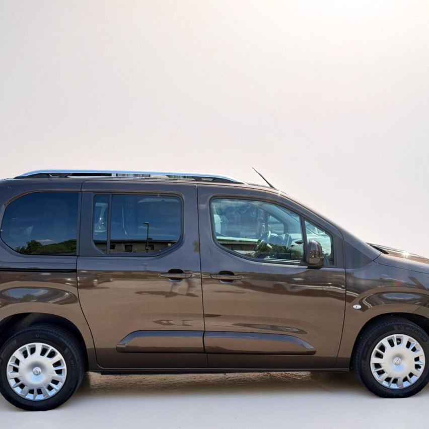 Ein brauner Van ist auf einer weißen Oberfläche geparkt, mit sichtbaren Seitenfenstern und einem klaren Himmel darüber.