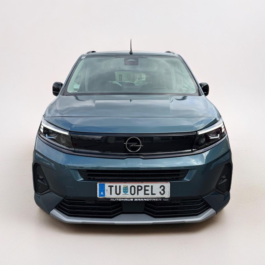 Frontansicht eines dunkelblauen Opel-Autos mit Nummernschild. Das Auto verfügt über moderne Scheinwerfer und einen Kühlergrill mit dem Opel-Logo. Das Fahrzeug steht in einem weiß umrandeten Bereich.