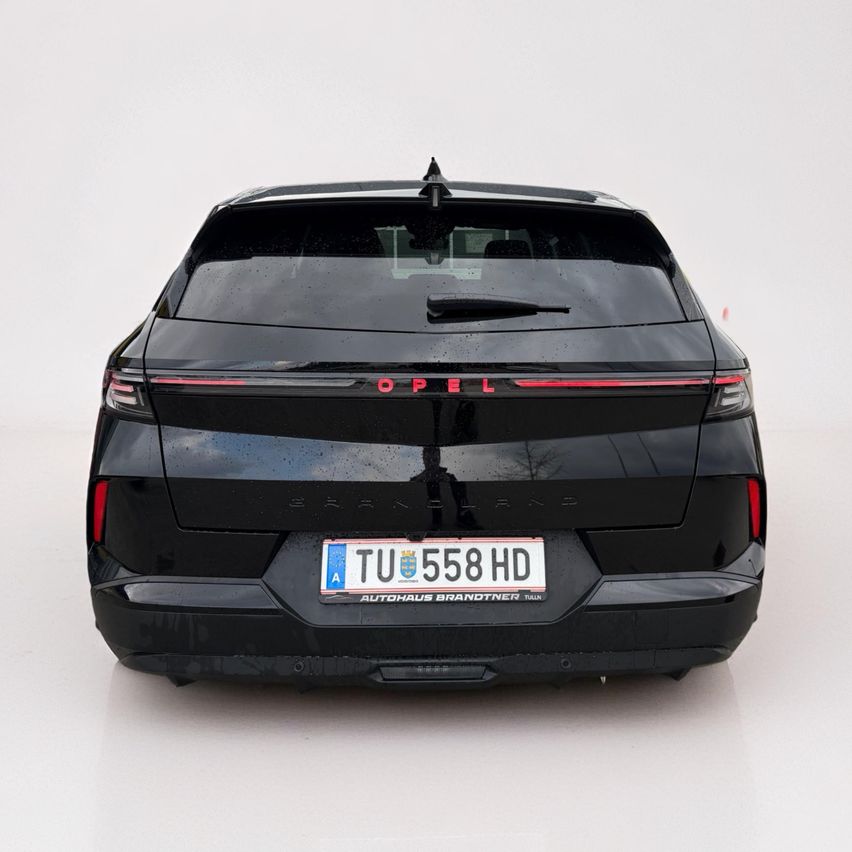 Rückansicht eines schwarzen Opel Grandland X SUV mit roter Lichtleiste, schwarzem Kennzeichen mit weißen Buchstaben und einer Reflexion auf der Scheibe.