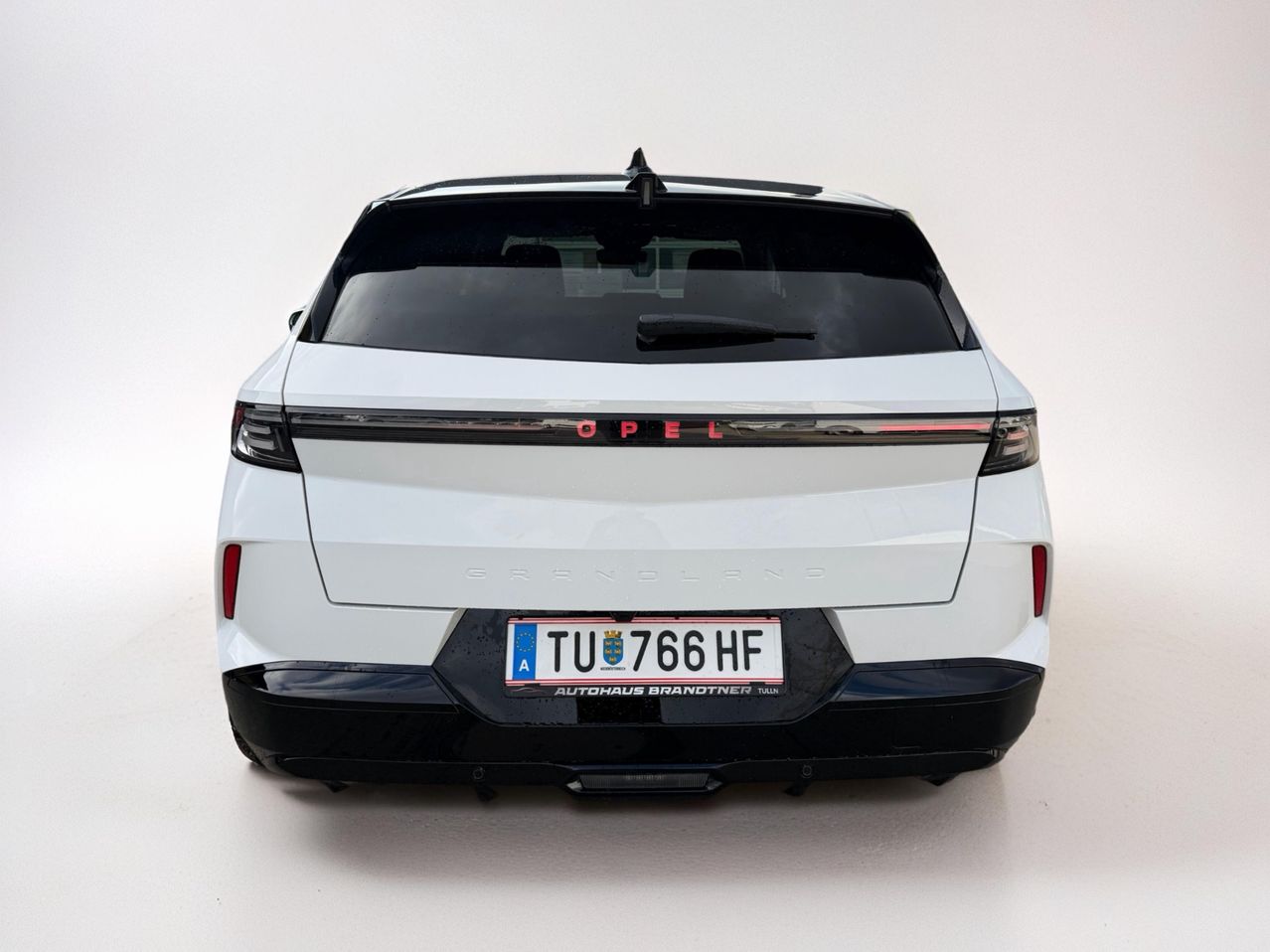 Die Rückseite eines weißen Opel Grandland SUV mit dem Nummernschild TU 766 HF. Der Heckspoiler und die Rückleuchten sind beleuchtet.