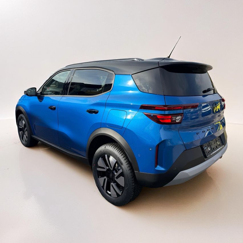 Die Rückseite eines blauen SUV mit Spoiler, Antenne und Nummernschild. Es wird in einem weißen Raum ausgestellt.