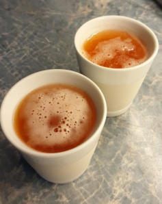 Zwei weiße Tassen, gefüllt mit einer braunen Flüssigkeit, wahrscheinlich Tee, stehen auf einer Marmoroberfläche. Die Flüssigkeit hat Blasen auf der Oberfläche, was darauf hindeutet, dass sie heiß ist.