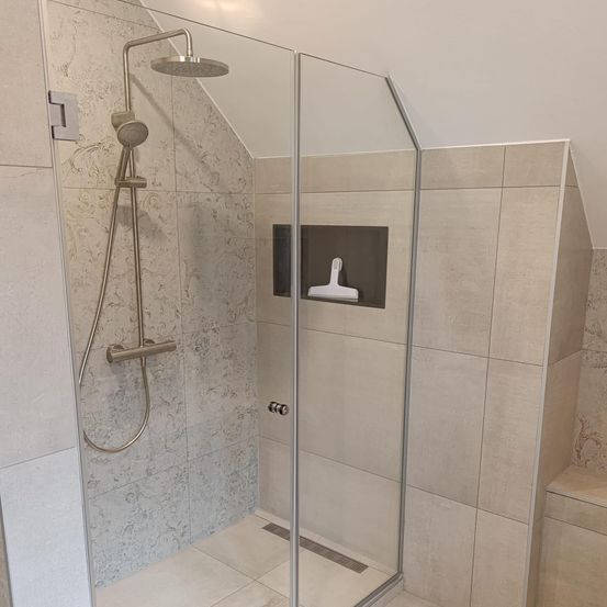 Ein moderner Duschbereich mit einer Glastür, gefliesten Wänden und einer eingebauten Duschbrause mit Schlauch. Die Duschbrause ist silber und die Wände sind beige mit Marmormuster.