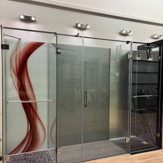 Eine moderne Duschkabine mit Glastüren, die eine rote abstrakte Gestaltung auf einer Seite aufweist. Die Kabine hat einen schlanken, metallischen Griff und einen silbernen Metallrahmen. Der Duschbereich ist durch eine zweite Glastür getrennt.