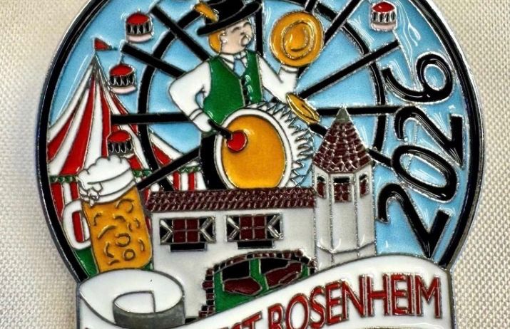 Eine Anstecknadel zur Erinnerung an das Herbstfest 2022 in Rosenheim mit einem Mann, der eine Trommel spielt, einem Bierkrug, einem Riesenrad und einem Schloss.