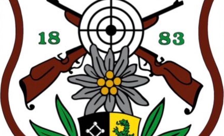 Das Emblem zeigt einen Schild mit einem Drachen und einem Schlüssel, flankiert von zwei Gewehre über einer Blume, mit den Zahlen 18 und 83 auf beiden Seiten.