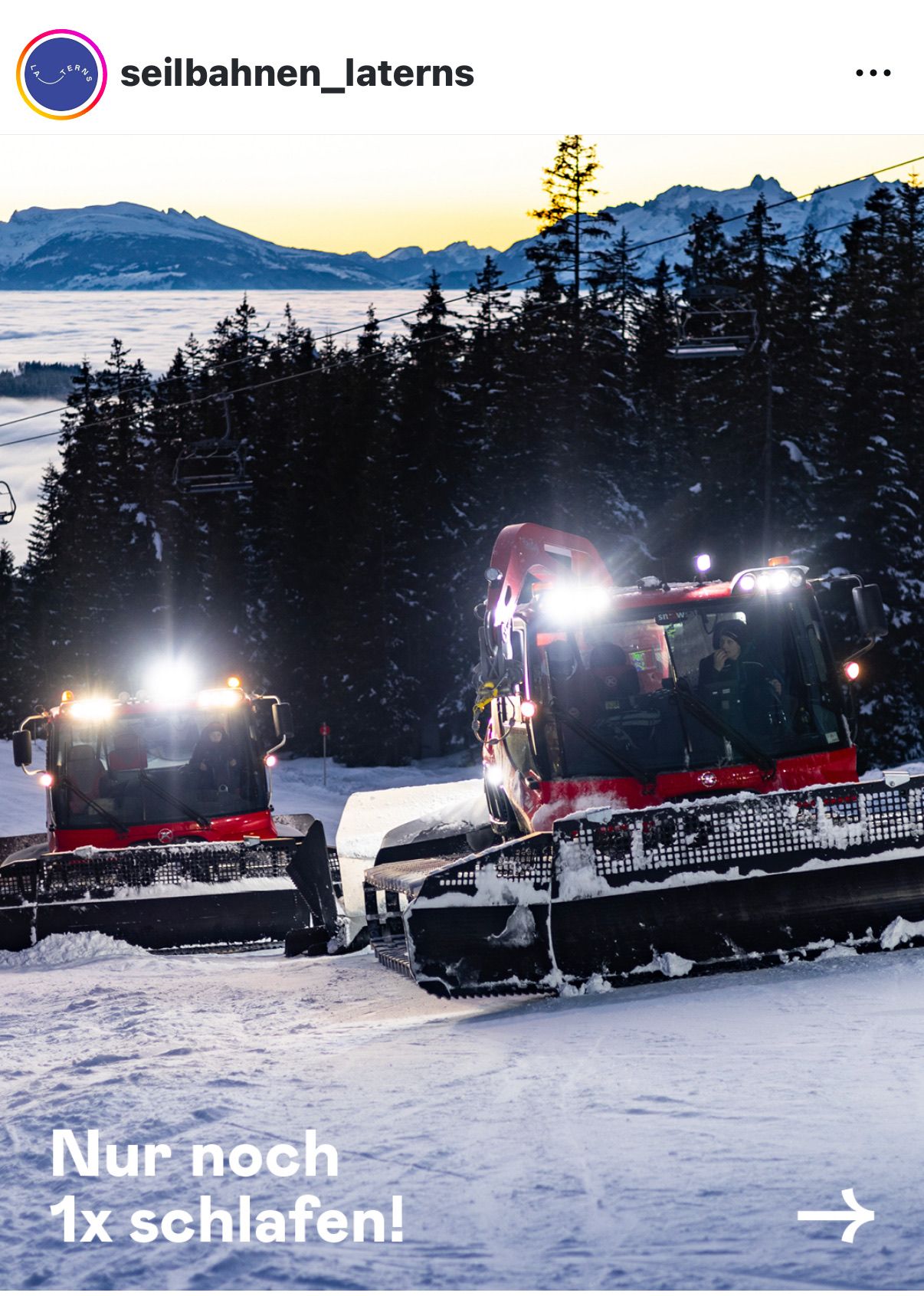 Zwei rote Schneepflüge räumen Schnee in einem bergigen, bewaldeten Gebiet unter einem untergehenden Sonnenuntergang.