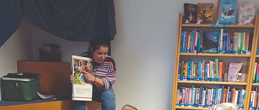 Eine Frau liest ein Buch für eine Gruppe von Kindern vor, die in einem Kreis in einer Bibliothek sitzen.