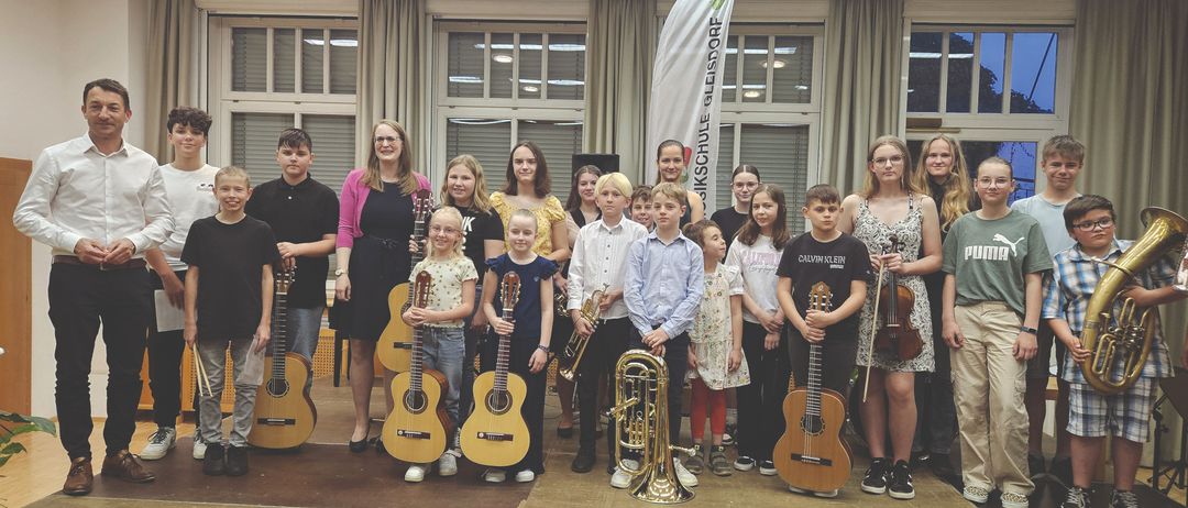 Eine Gruppe von Kindern und Erwachsenen, wahrscheinlich Musiker, stehen zusammen, halten Instrumente und posieren für ein Foto.