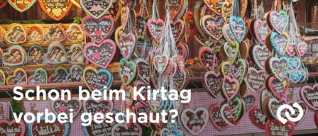 A display of heart-shaped cookies decorated with various messages hangs from the ceiling, likely at a Christmas market. The cookies are in different colors and sizes, with some featuring hearts and others having text. The background is blurred.