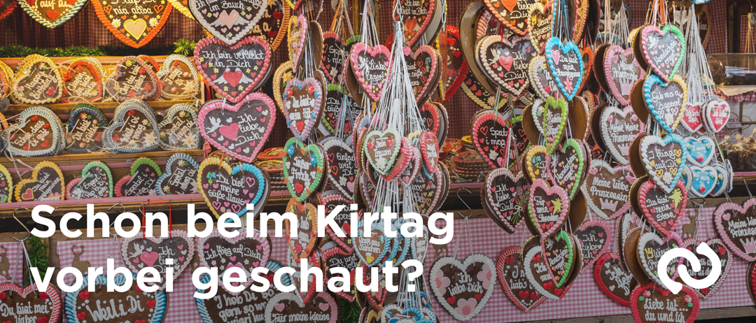 A display of heart-shaped cookies decorated with various messages hangs from the ceiling, likely at a Christmas market. The cookies are in different colors and sizes, with some featuring hearts and others having text. The background is blurred.