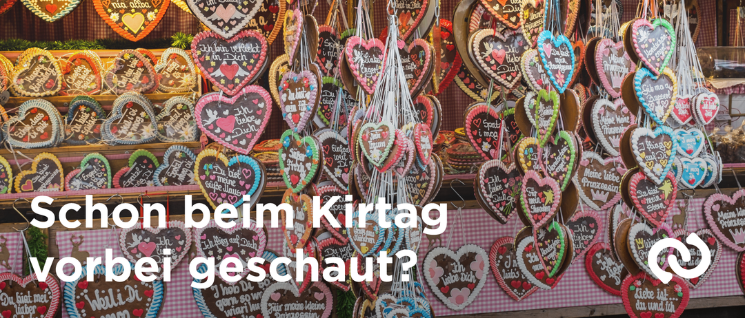 Eine Ausstellung von herzförmigen Keksen mit dekorativer Beschriftung, die an Fäden hängen, vor einem rosa-weiß karierten Hintergrund.