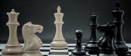 Ein Schachbrett mit einem weißen König in der Mitte und anderen Figuren darum herum. Die Figuren stehen vor einem schwarzen Hintergrund.