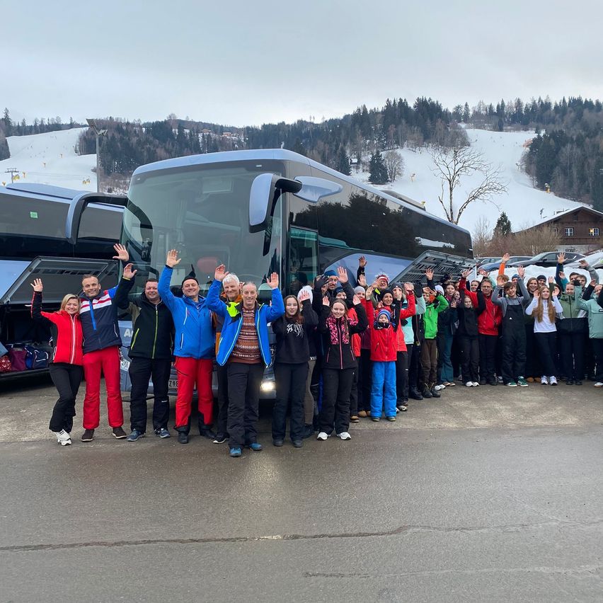 Eine Gruppe von Menschen steht vor einem Bus in einer verschneiten Landschaft, alle in Winterkleidung.