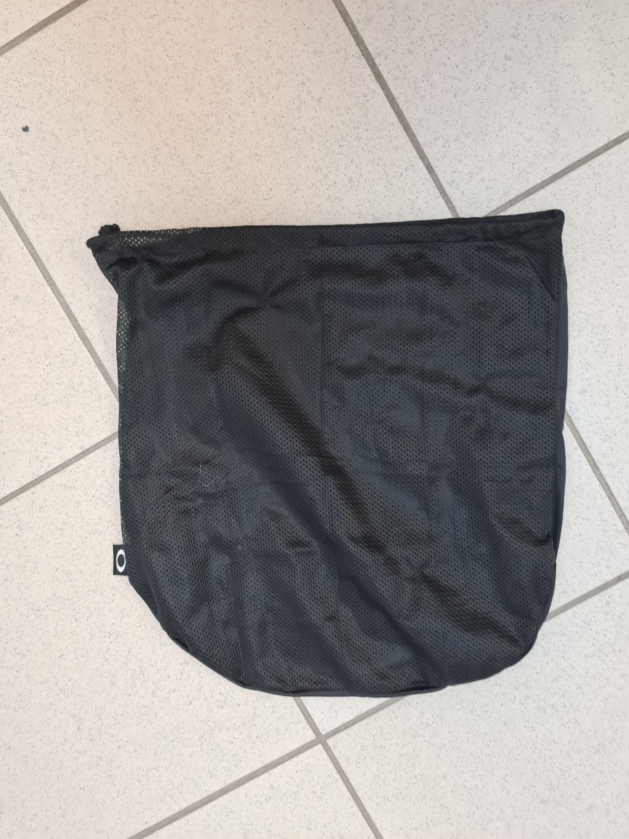 A black mesh bag with a small logo is laid flat on a tiled floor.