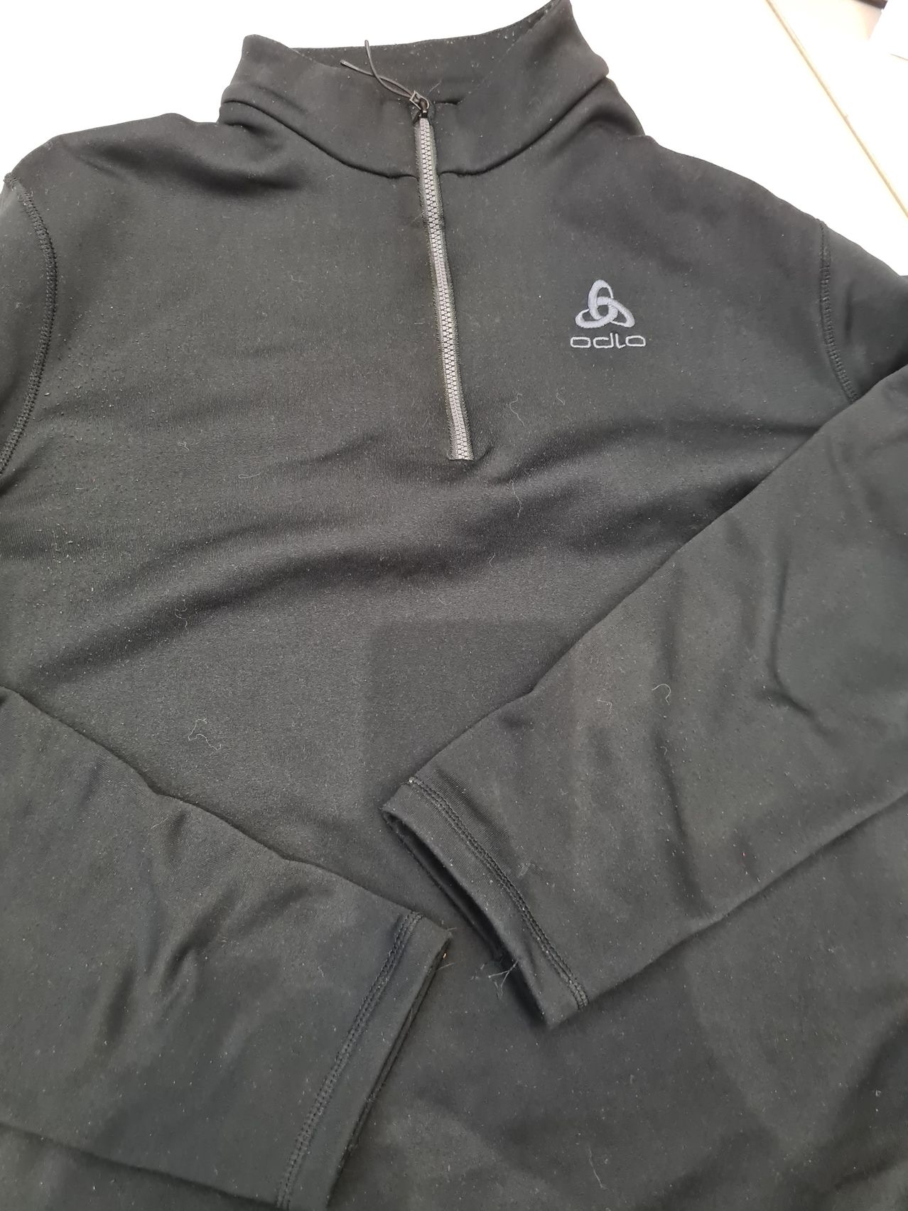 A black hoodie with a zipper, displaying a white logo on the left chest area. The sleeves and hem are slightly frayed.