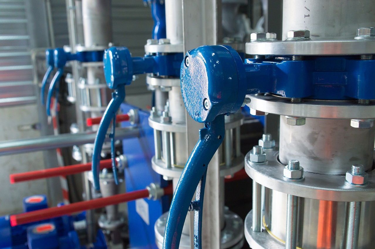 Nahaufnahme von blauen und silbernen Industrieventilen und Rohren, mit roten Rohren im Hintergrund.