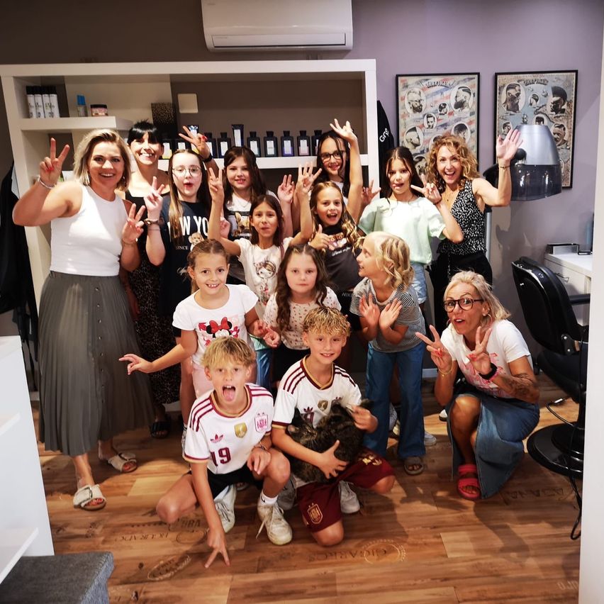 Eine Gruppe von Frauen und Kindern posiert für ein Foto in einem Salon, einige machen Friedenszeichen.