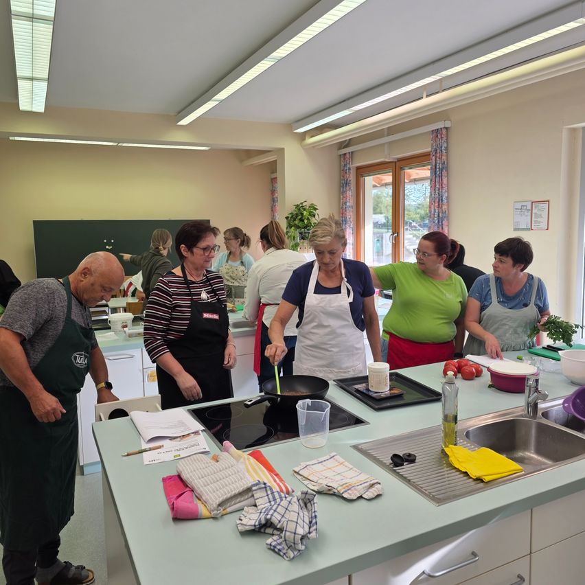 Eine Gruppe von Menschen in einer Küche, einige tragen Schürzen und scheinen zu kochen.