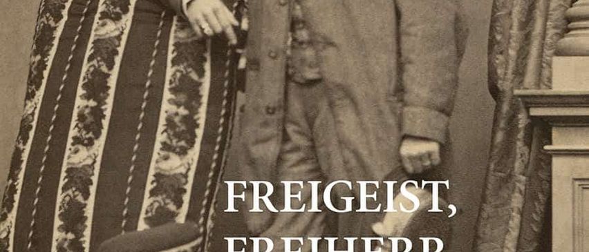 Schwarz-Weiß-Foto eines Mannes, der neben einem Stuhl steht. Er trägt einen Mantel mit einer Fliege. Der Text lautet 'Freigeist, Freiherr, Fabrikant' und der Name Carl Maria Joseph Leopold von Seyffertitz.
