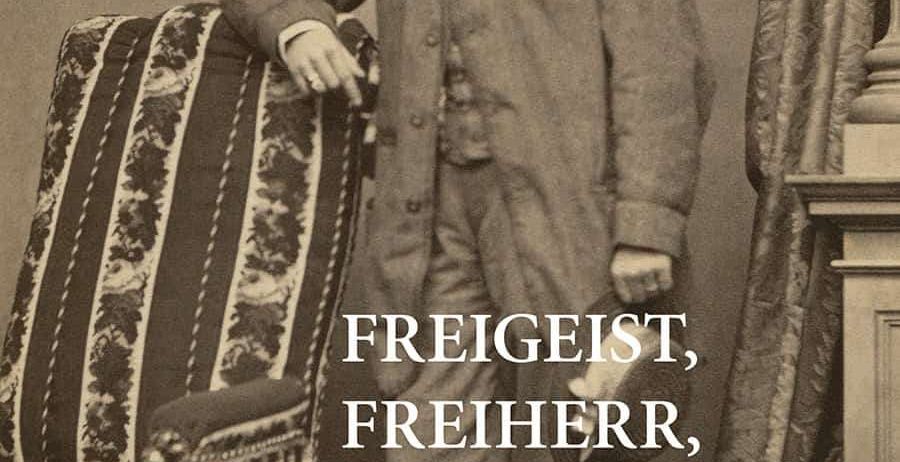 Schwarz-Weiß-Foto eines Mannes, der neben einem Stuhl steht. Er trägt einen Mantel mit einer Fliege. Der Text lautet 'Freigeist, Freiherr, Fabrikant' und der Name Carl Maria Joseph Leopold von Seyffertitz.